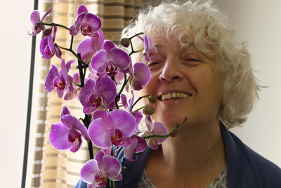 Senior woman holding a lilac orchid and smiling at the camera. close-up of woman with flowers.