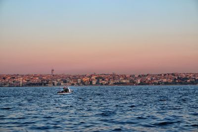 Sailboats in sea by buildings against sky during sunset