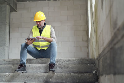 Side view of man using mobile phone while standing against wall