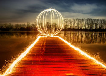 Illuminated ferris wheel by lake against sky at night