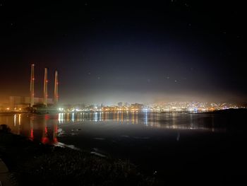 Illuminated city by river against sky at night