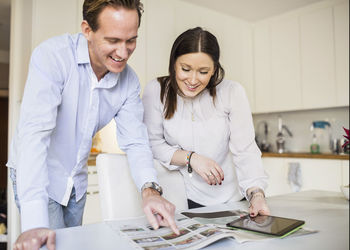 Happy couple with digital tablet looking at catalog in kitchen