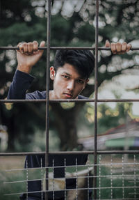 Portrait of young man looking through metal fence