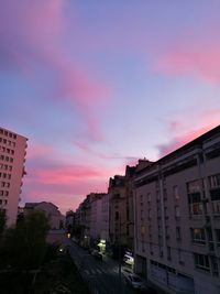 Cars on road by buildings against sky during sunset