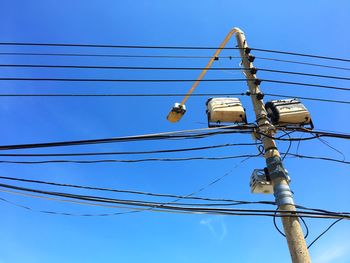 Low angle view of street light with electricity cables against blue sky