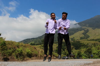 Friends jumping over ground against mountain