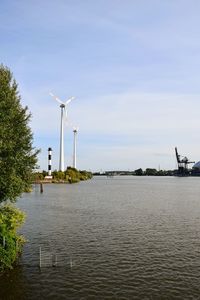 Wind turbines by lake against sky