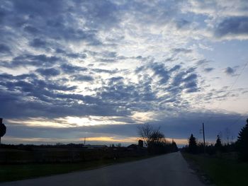 Road amidst silhouette trees against sky