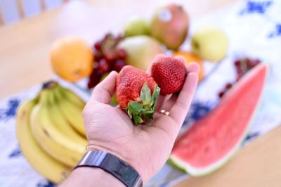 Close-up of cropped hand holding strawberries at home