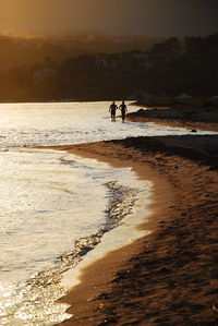 High angle view of man and woman walking at beach during sunset