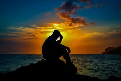 Silhouette man on sea against sky during sunset