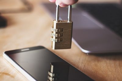 Close-up of person holding padlock over smart phone on table