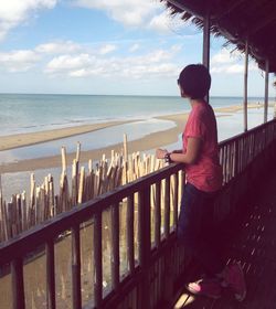 Side view of woman standing by railing at balcony against sea