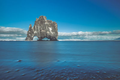 View of rock formation in sea against blue sky
