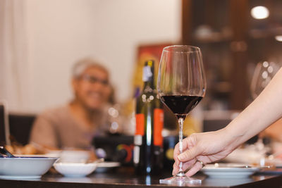 Woman holding glass red wine on dinner table.