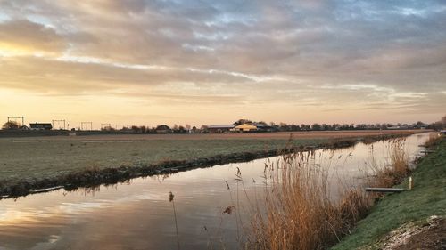 Scenic view of lake against cloudy sky at sunset