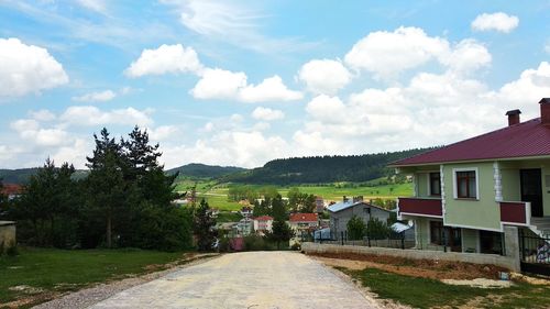 Road amidst trees and buildings against sky