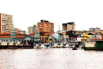 Boats in river by buildings against clear sky