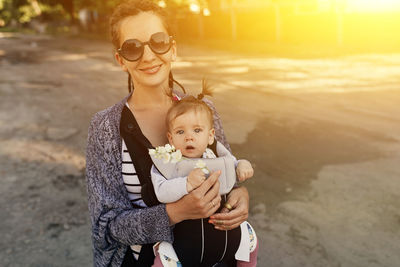 Portrait of happy mother carrying daughter while standing outdoors during sunset