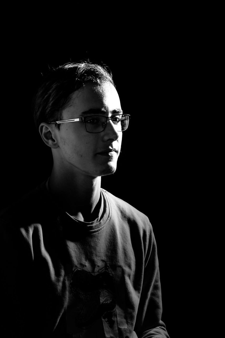 portrait, one person, black background, studio shot, glasses, headshot, young adult, young men, boys, indoors, casual clothing, eyeglasses, front view, males, lifestyles, men, serious, looking away, teenager, teenage boys, adolescence, contemplation