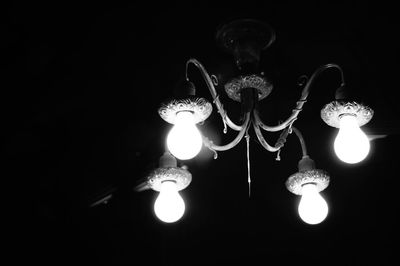 Close-up of illuminated lighting equipment hanging against black background