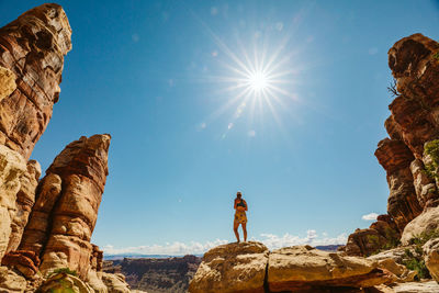 Woman in sports bra and shorts stands on rocks in desert under sun