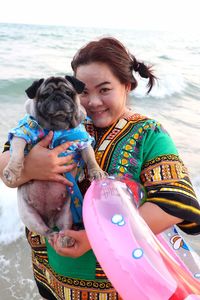 Portrait of woman holding pug at beach