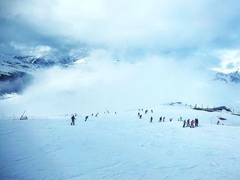 People on snow covered field against sky during winter