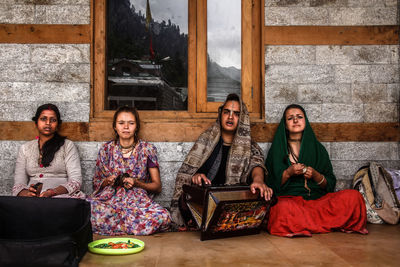 Pilgrims sitting with harmonium against wall at temple