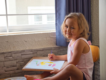 Side view portrait of girl drawing on paper while sitting on chair at home