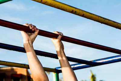 Cropped image of person holding horizontal bar against sky