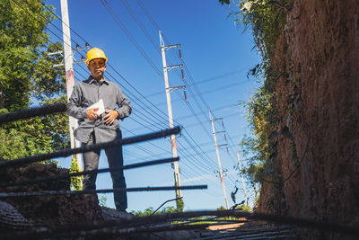 Low angle view of man working on electricity pylon against sky