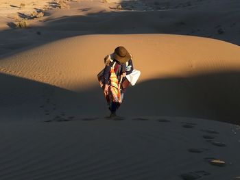 High angle view of woman wearing hat while walking on sand at desert