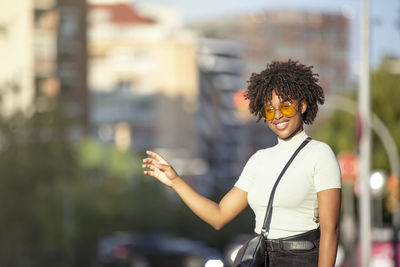 Beautiful afro-haired young woman standing on the street and taking a taxi with her hand up