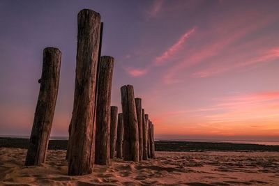 Wooden posts on beach against sky during sunset