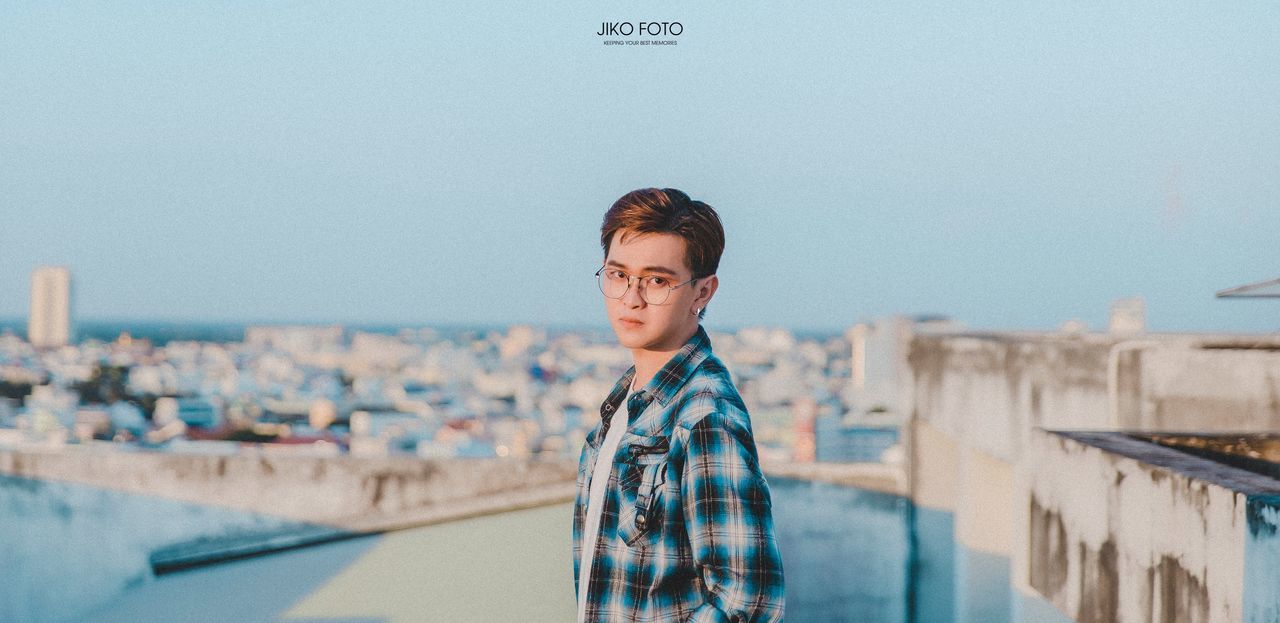 architecture, one person, real people, built structure, building exterior, young adult, portrait, sky, focus on foreground, lifestyles, casual clothing, looking at camera, waist up, leisure activity, young men, standing, nature, front view, outdoors, cityscape, contemplation
