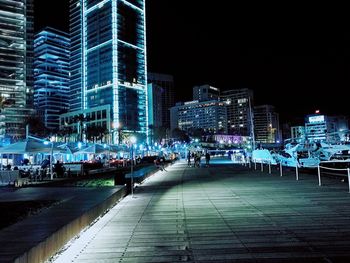 People on illuminated street amidst buildings in city at night