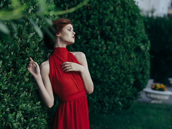 Young woman looking away while standing against plants