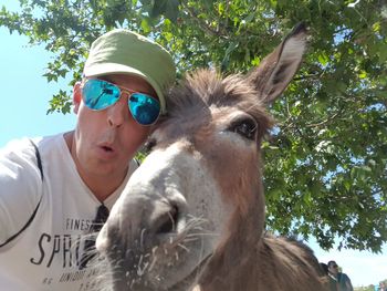 Man wearing sunglasses while taking selfie with donkey against trees