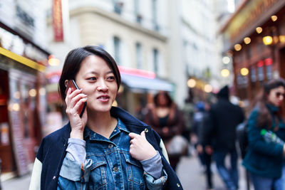 Young woman using phone while standing on street in city