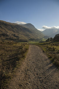 Dirt road amidst landscape against sky