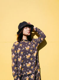 Portrait of mid adult woman wearing hat while standing against yellow wall