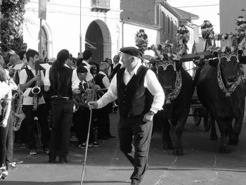 Man with walking cane by musicians and bulls on street during traditional festival in city