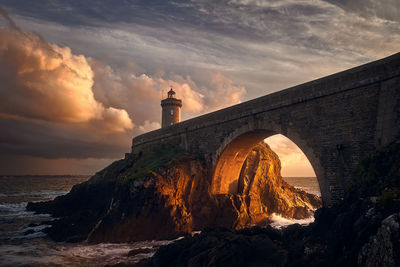 Arch pier by phare du petit minou by sea against cloudy sky