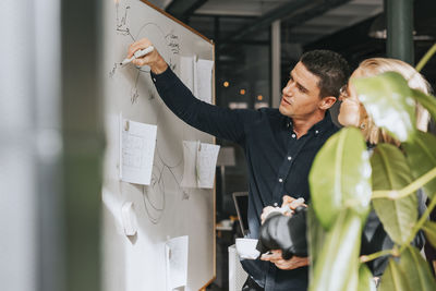 Businessman writing on white board while discussing with female colleague at office