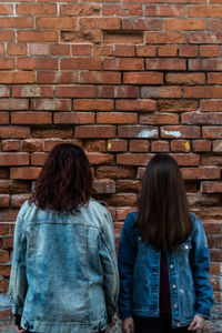 Rear view of women standing against brick wall