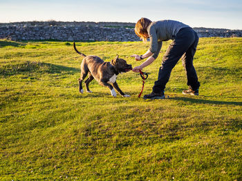 Full length of mature woman playing with dog on grass