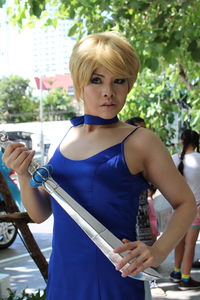 Young woman in costume holding sward while standing on footpath in city