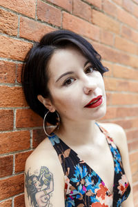 Portrait of young woman standing against brick wall