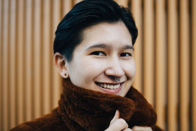 Portrait of smiling woman against wooden wall